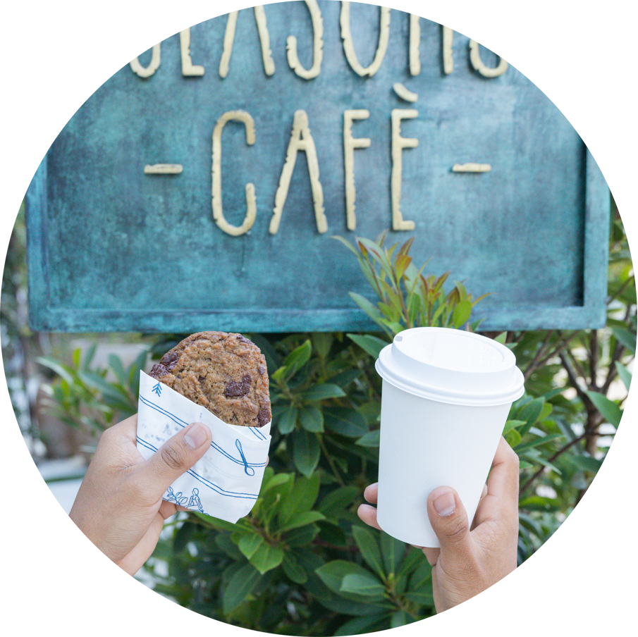 Showcasing coffee and a chocolate chip cookie in front of the Seasons Cafe's signage.